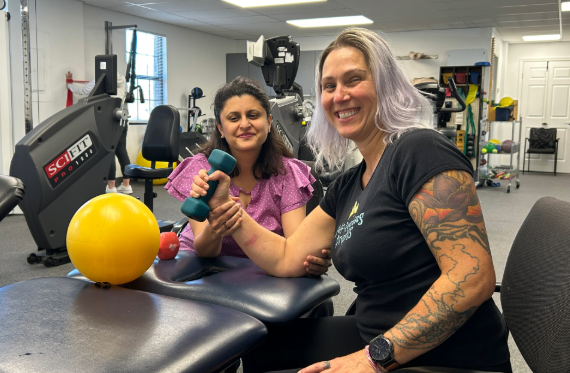 Cindy smiles at the camera while working on arm strength with her therapist.