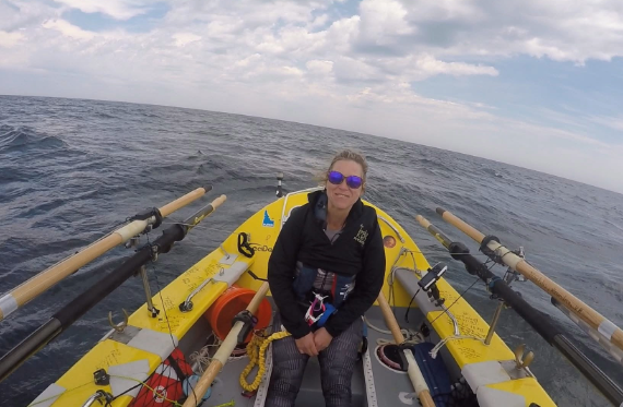 Cindy looks at the camera in smiles sitting in a boat surrounded by open water.